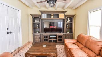 A living room with a television, wooden cabinets, a ceiling fan, and a sofa.
