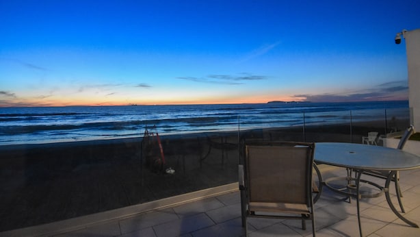 Una terraza con vistas al océano al atardecer, con una mesa y sillas.