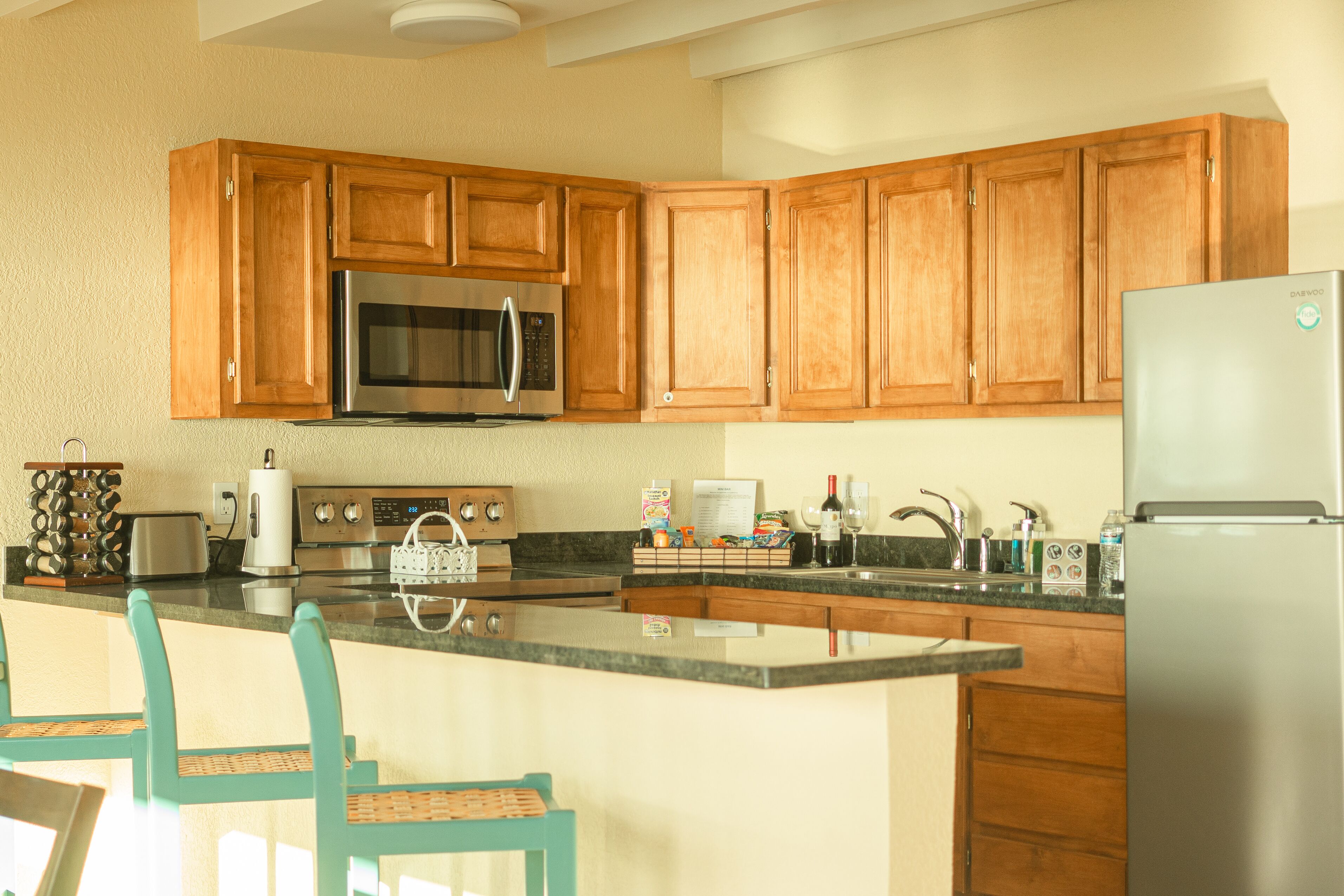 Una cocina con armarios de madera, electrodomésticos de acero inoxidable, encimera de granito y sillas color turquesa.