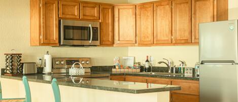 Una cocina con armarios de madera, electrodomésticos de acero inoxidable, encimera de granito y sillas color turquesa.
