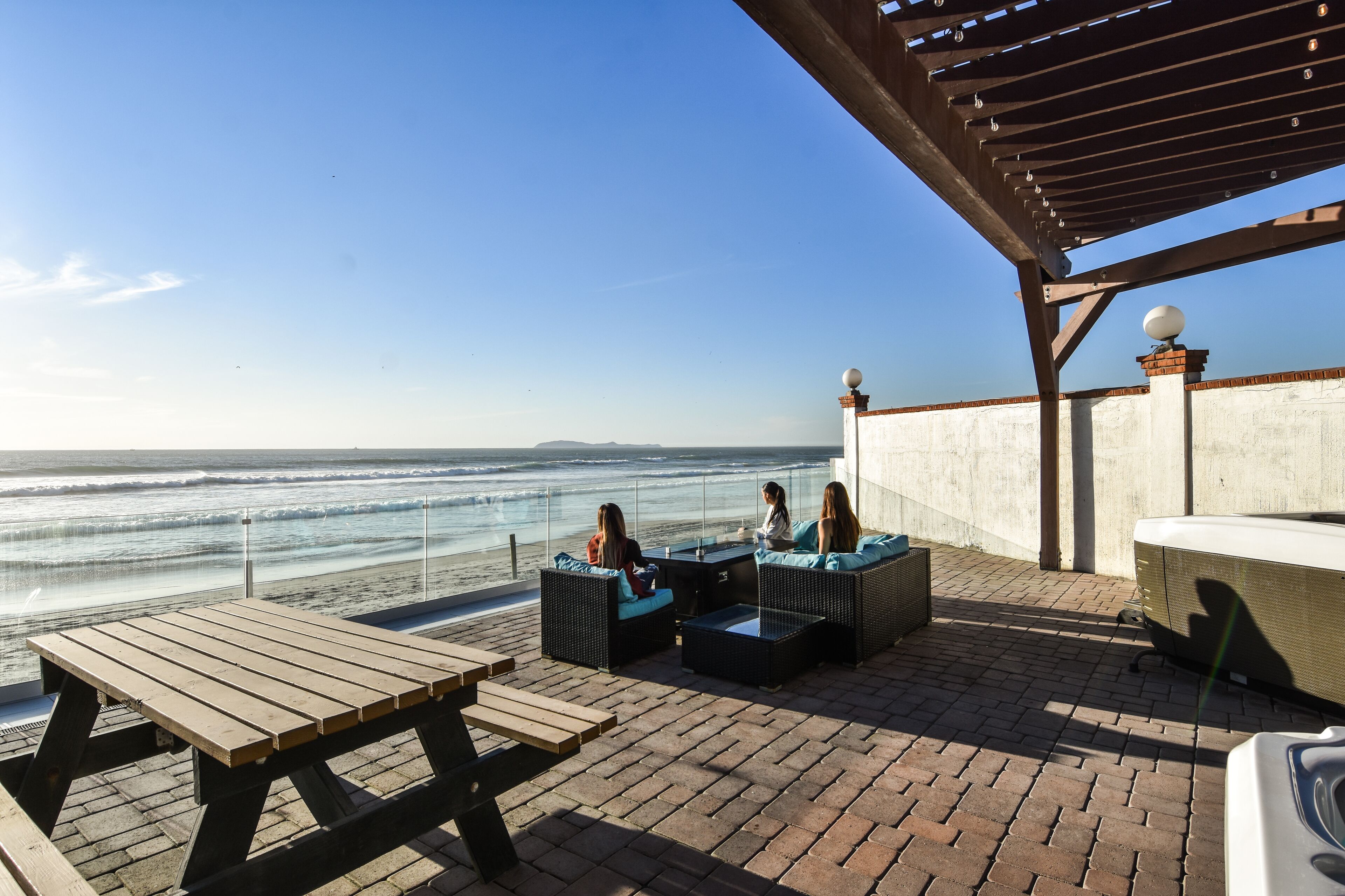 A patio with outdoor seating overlooking the ocean, a wooden table, and a pergola structure.