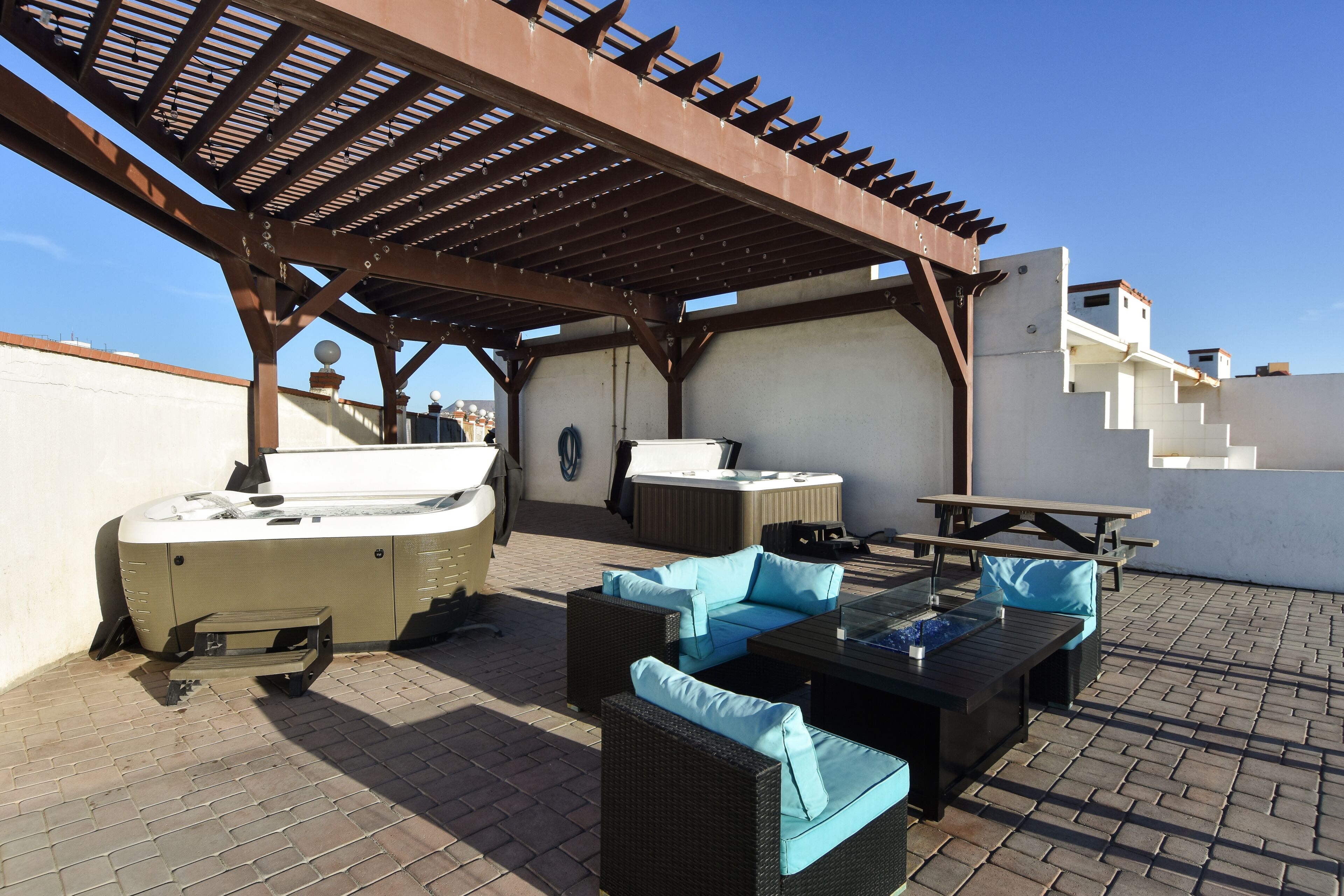 Un patio exterior con pérgola, zona de estar, jacuzzi y una escalera que lleva a niveles superiores.