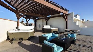 Un patio exterior con pérgola, zona de estar, jacuzzi y una escalera que lleva a niveles superiores.