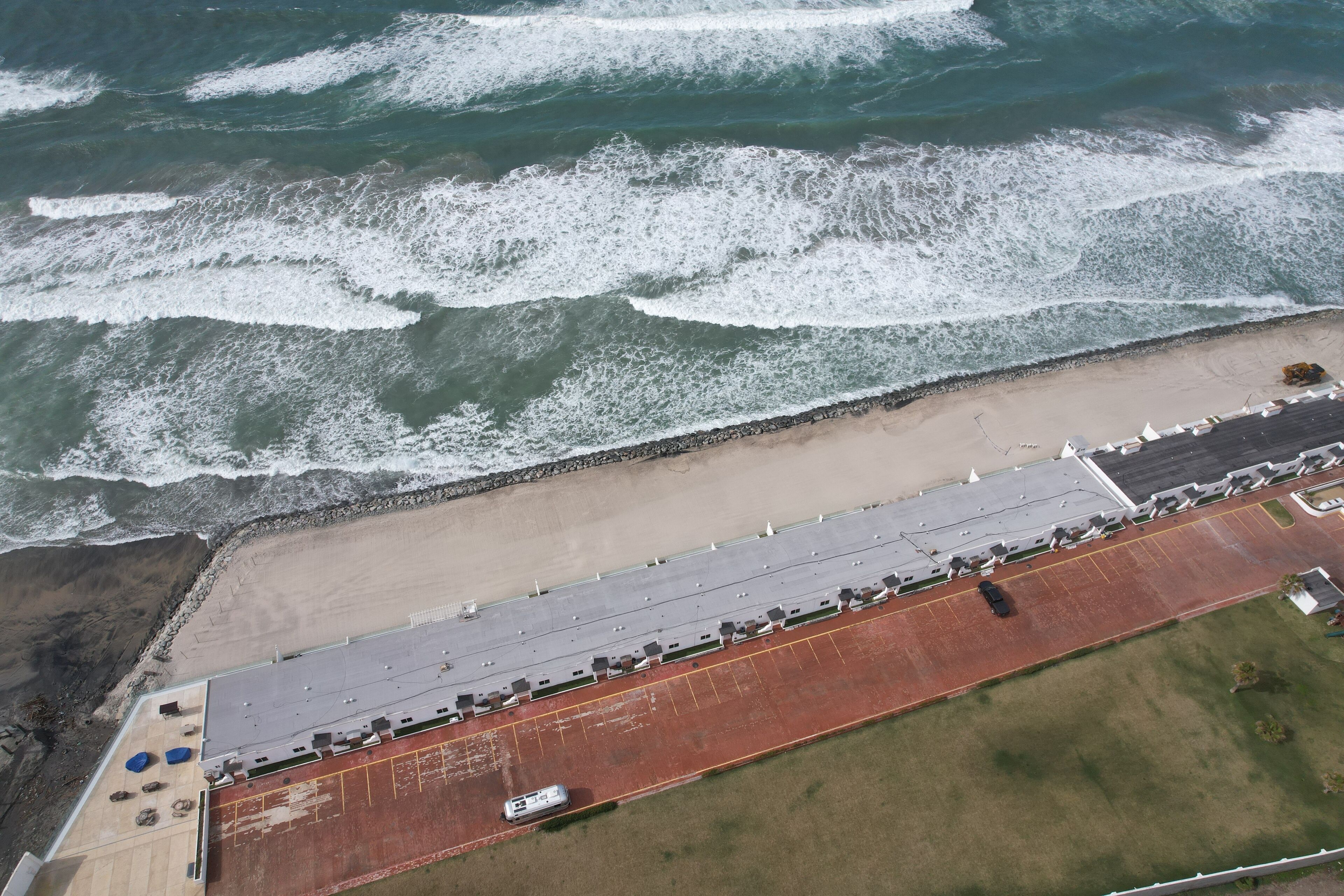 An aerial view of a coastal building with a parking lot and a beach.