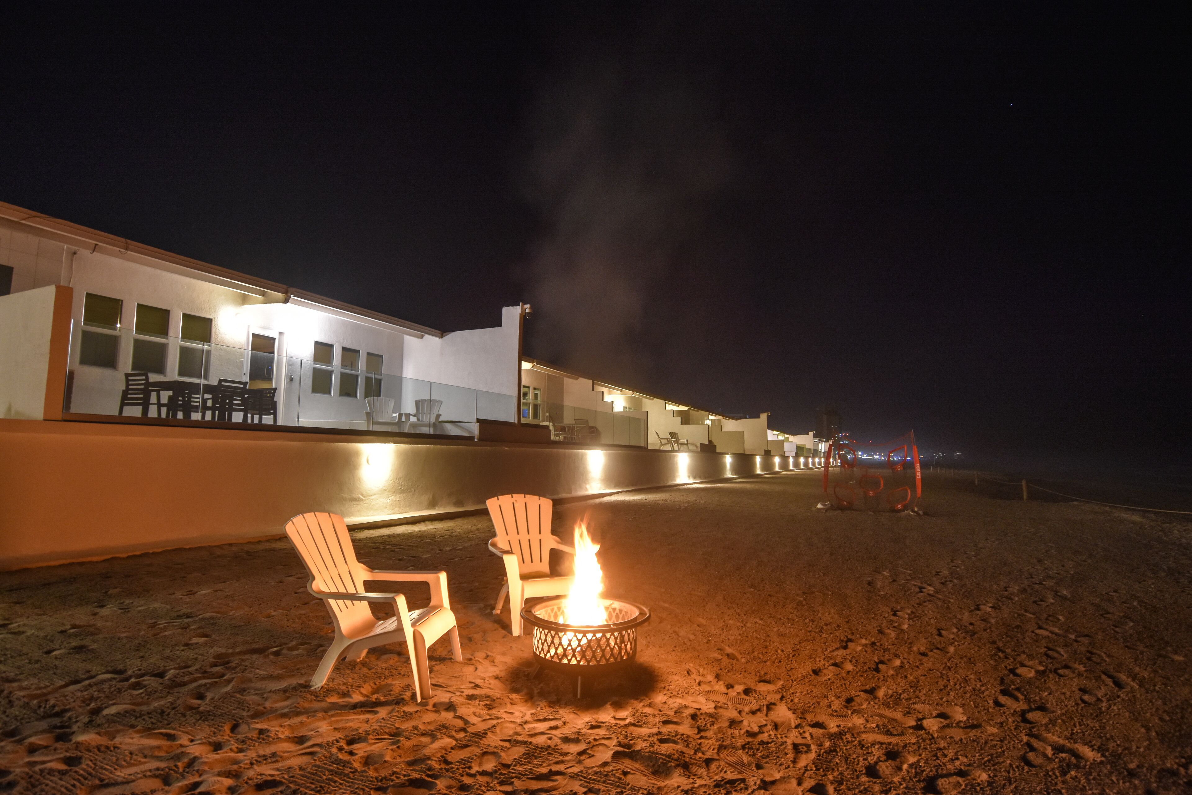 Un espace aménagé avec des sièges, un foyer et des chaises, situé en bord de plage et offrant une vue sur celle-ci.