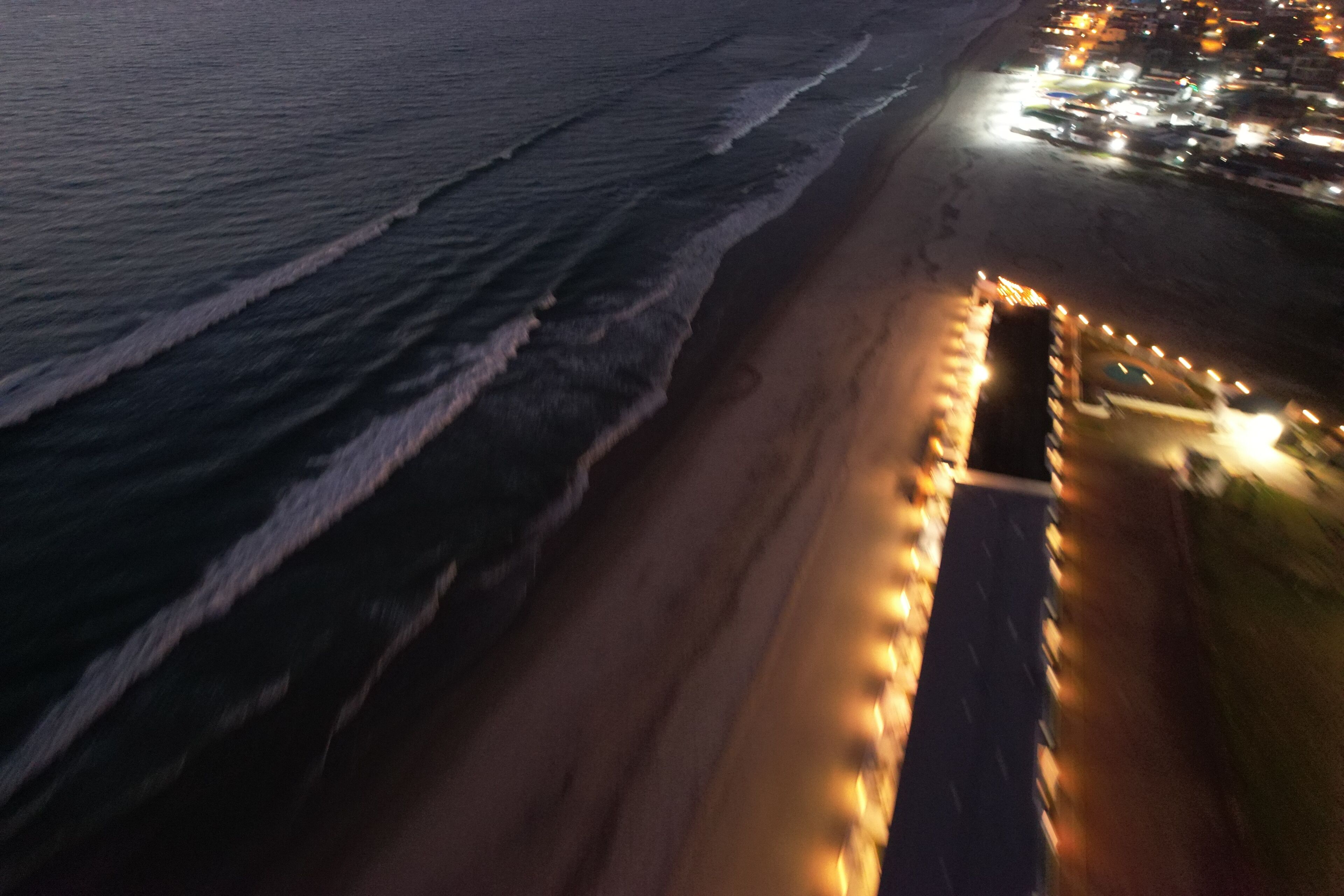 A beach with a row of lights along the shoreline, a sandy beach, and a calm sea.