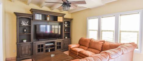 A living room with a leather sofa, a wooden coffee table, a TV on a wooden stand, and a ceiling fan.