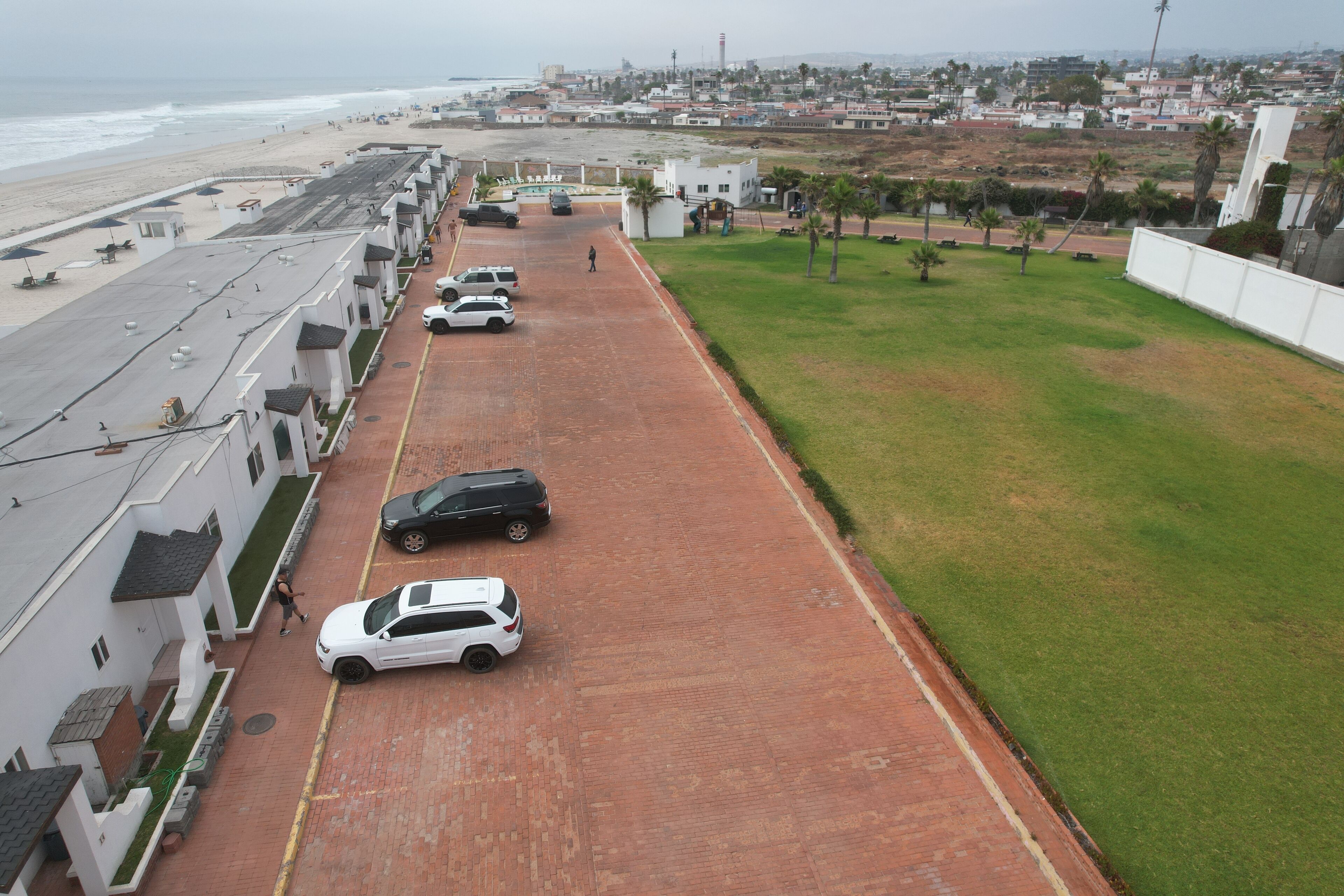 Una carretera costera con autos estacionados, un peatón y edificios a lo largo de la playa.