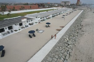 A beachside hotel with outdoor seating and umbrellas, a concrete walkway, and a rocky shoreline.