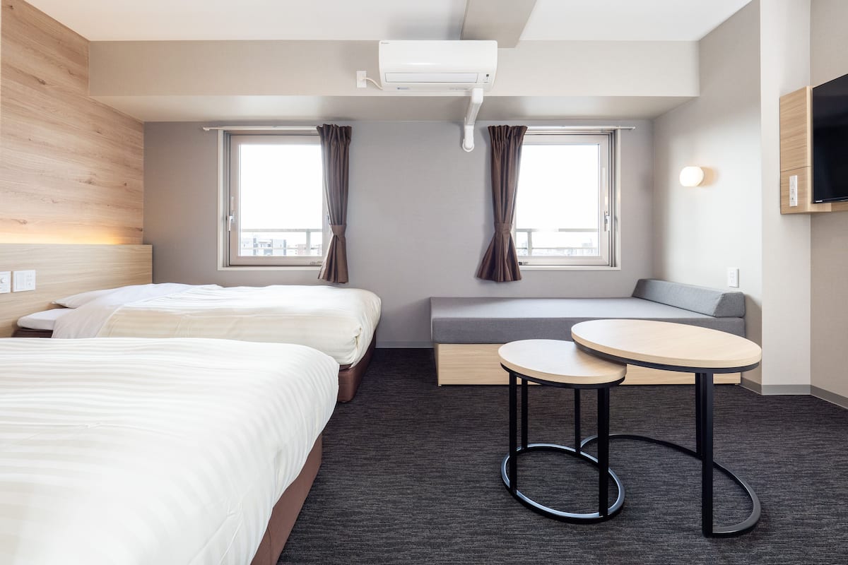 Una habitación de hotel con dos camas, un sofá, una mesita y un televisor.