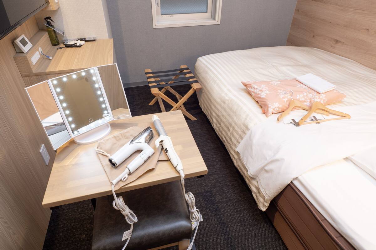 Una habitación de hotel con una cama, un tocador con espejo, un escritorio con lámpara y una silla.