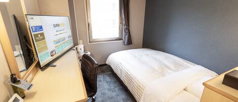 A hotel room with a bed, a desk with a computer, a chair, a window with curtains, and an air conditioning unit.