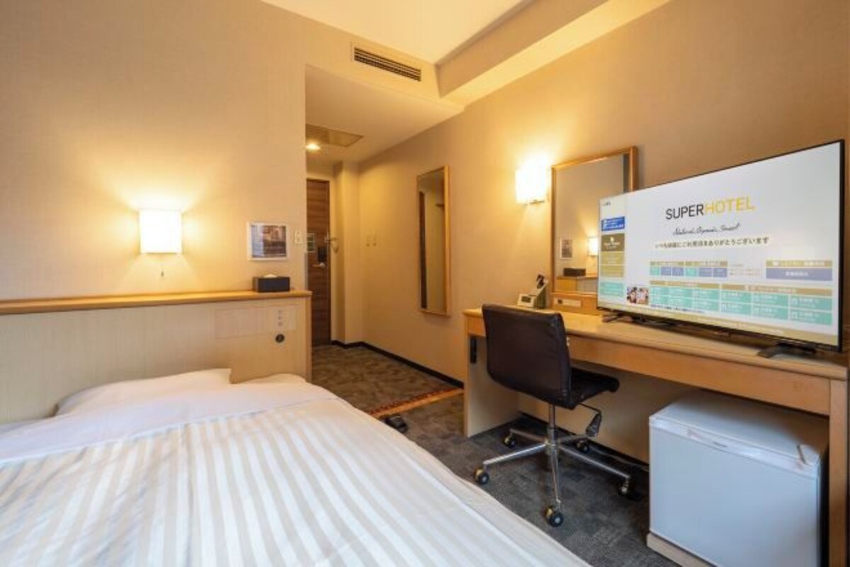 Habitación de hotel con cama, escritorio, silla y una pantalla grande que muestra información de la habitación.