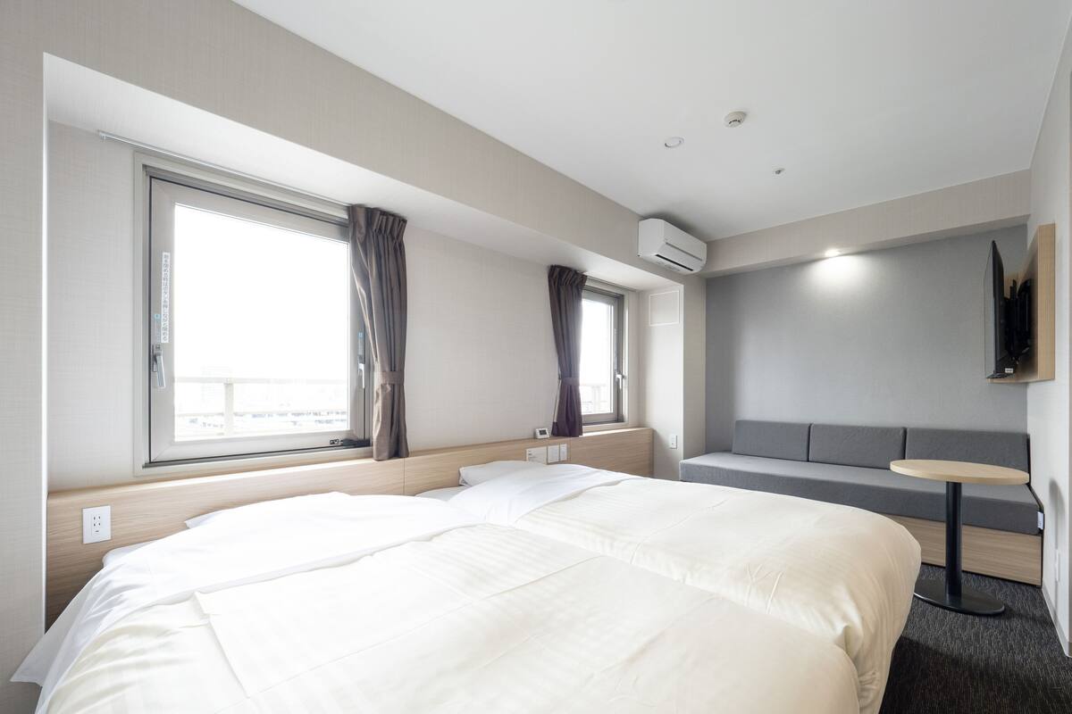 Una habitación de hotel con una cama grande, un sofá, una mesita y un ventanal con cortinas.