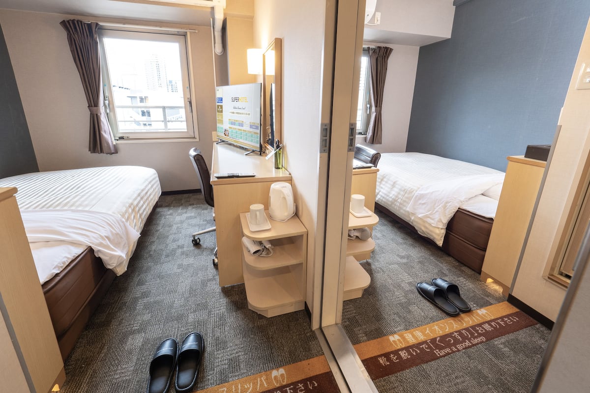 Habitación de hotel con dos camas, un escritorio, una silla, un espejo y una ventana.