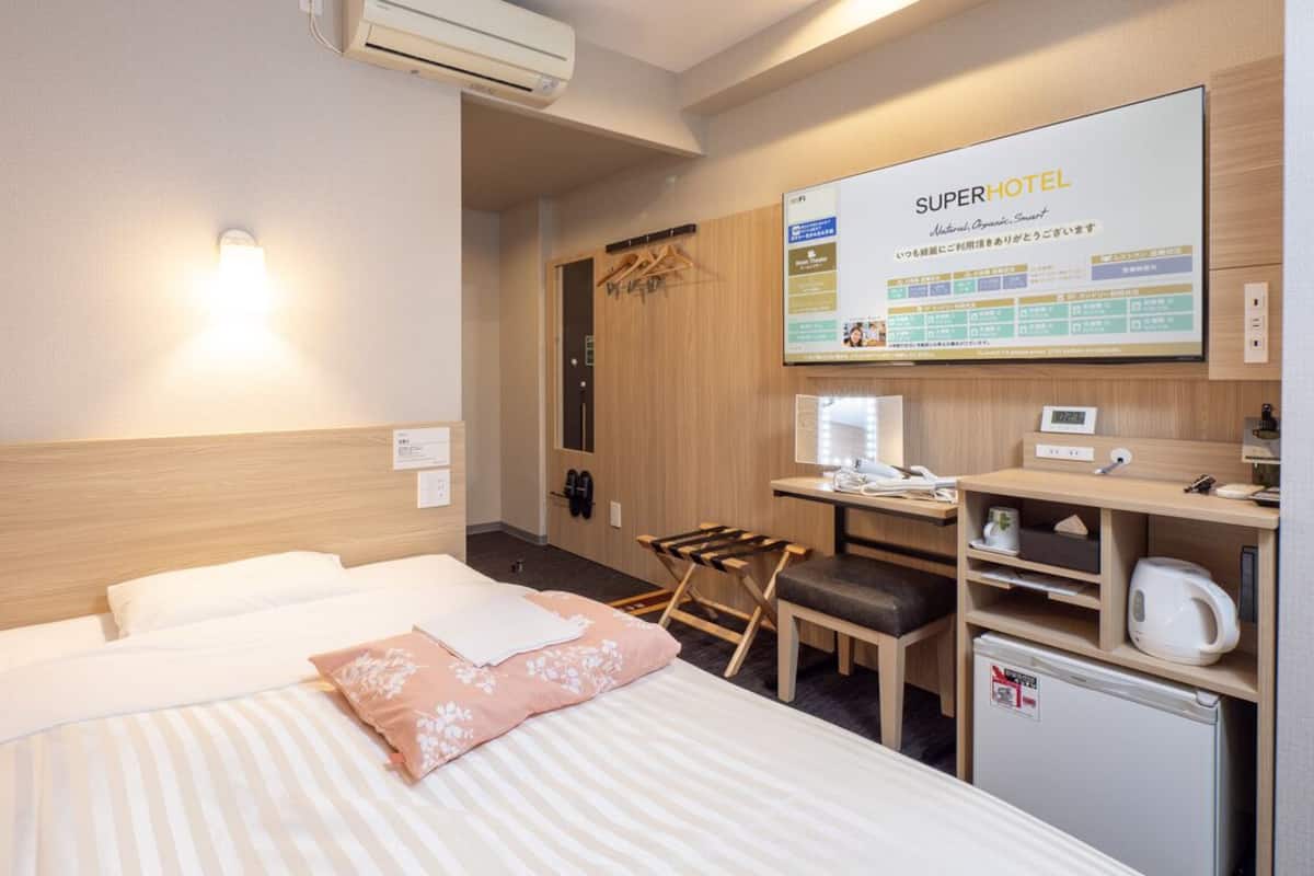 Habitación de hotel con dos camas, un escritorio, una silla, un refrigerador pequeño y un televisor de pared que muestra información del hotel.