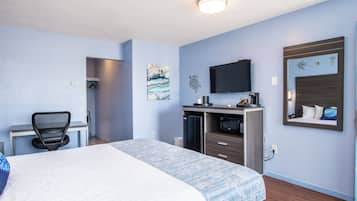 A hotel room with a bed, desk, chair, TV, and a small kitchenette.