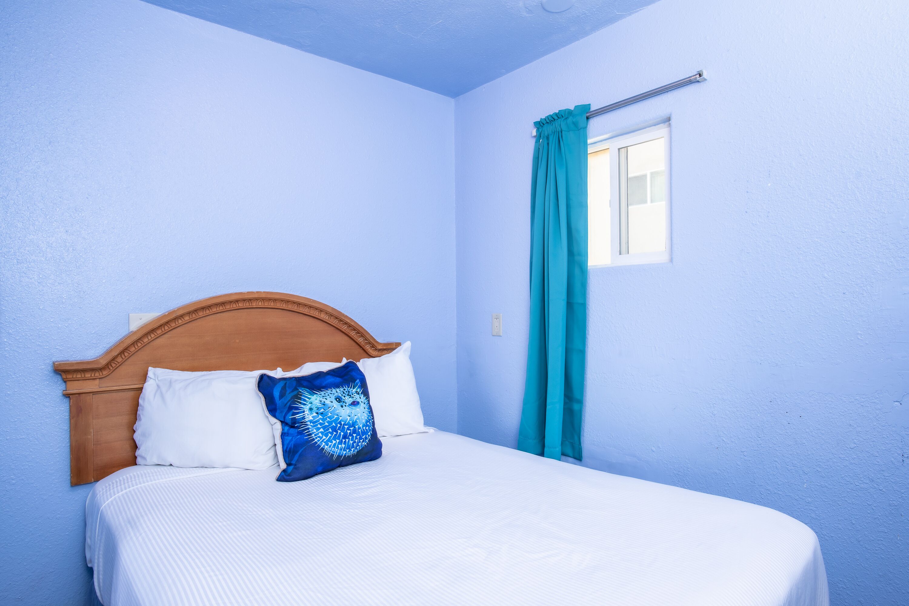 A bed with a wooden headboard, white bedding, and a blue patterned pillow.