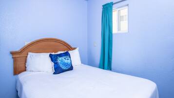A bed with a wooden headboard, white bedding, and a blue patterned pillow.