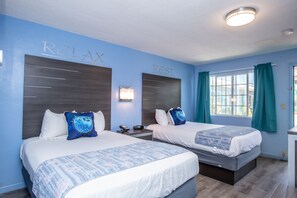 A hotel room with two beds, a nightstand, a lamp, and a window with curtains. - Aqua Breeze Inn (Santa Cruz)