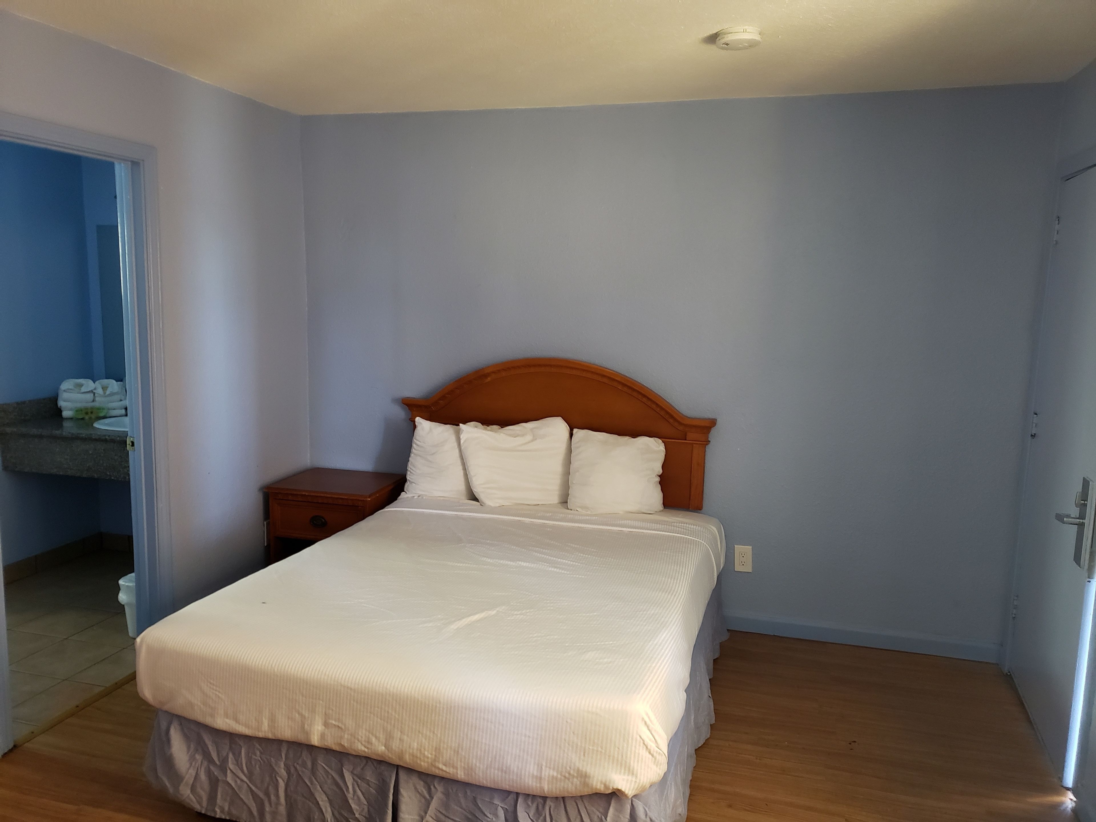A bedroom with a wooden bed, a nightstand, and a bathroom visible through an open door.