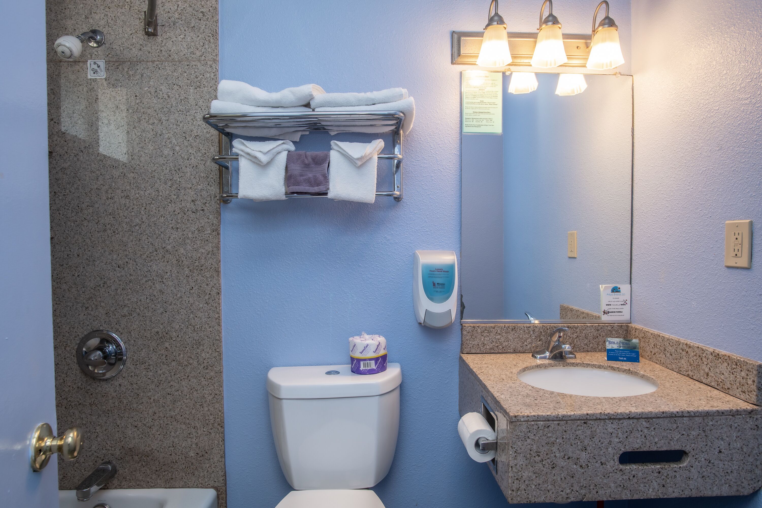A bathroom with a sink, toilet, towel rack, and a mirror with lights.