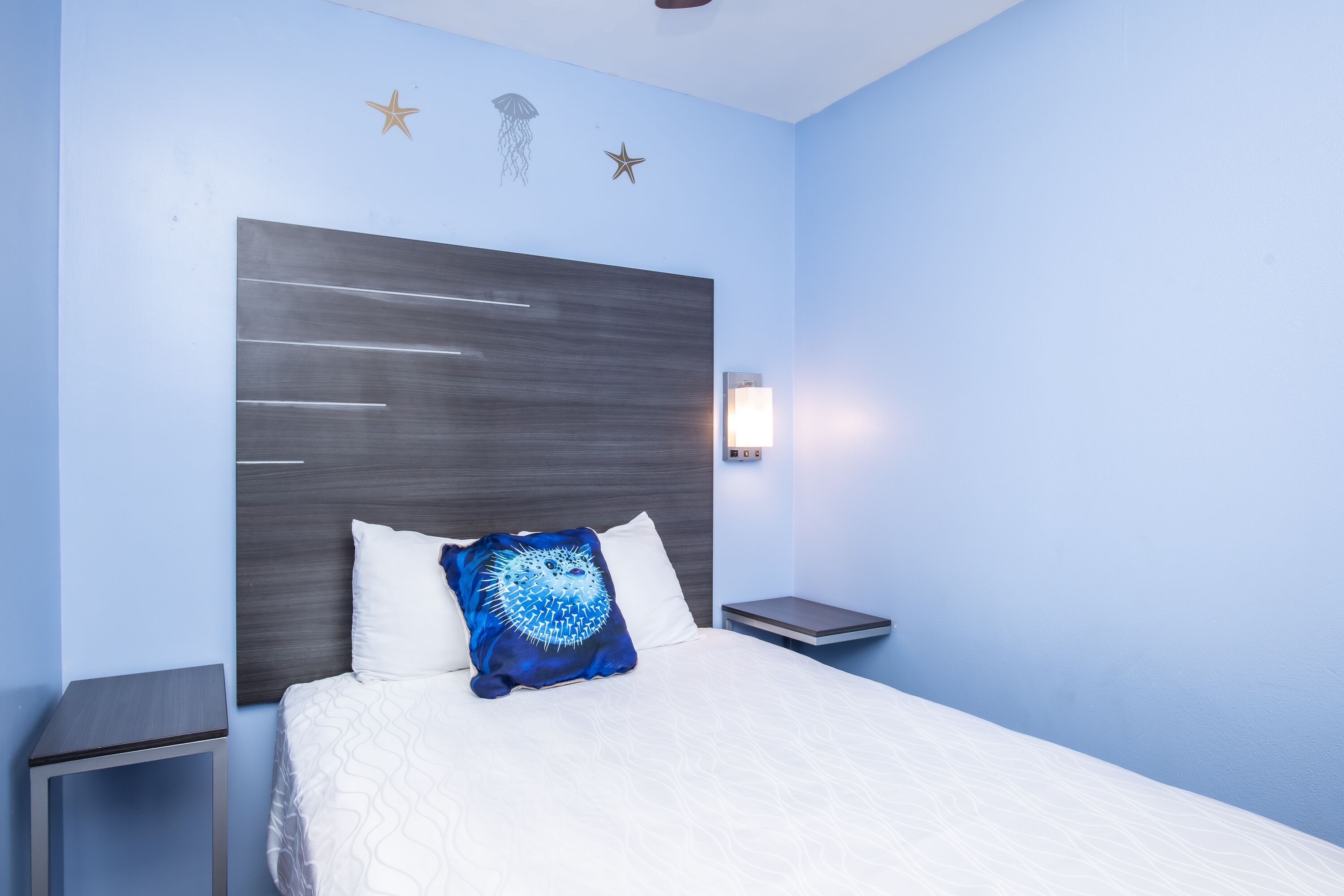 Ein Schlafzimmer mit einem Bett, einem Nachttisch, einer Wandlampe und dekorativen Wandbildern von Sternen und Quallen.