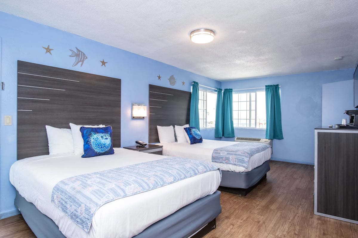Hotellihuone, jossa on kaksi sänkyä, työpöytä ja ikkuna, jossa on verhot.