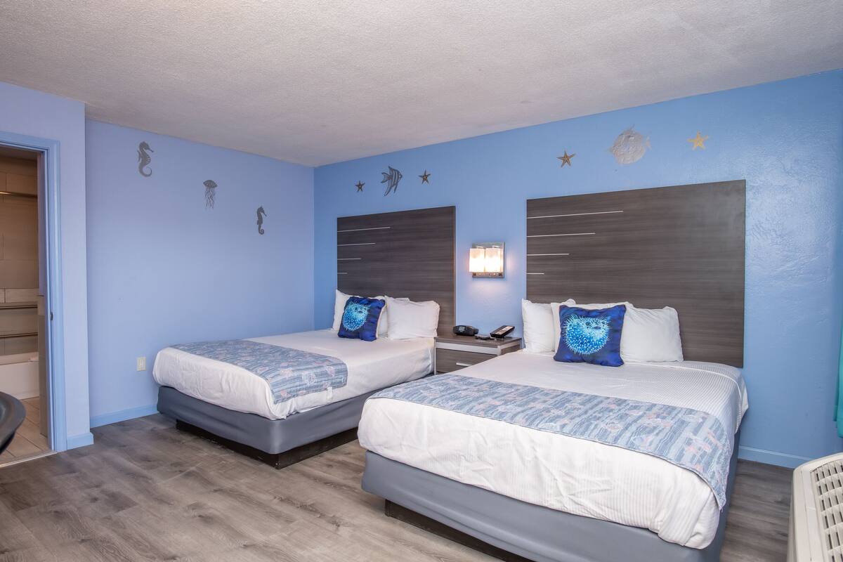 Hotellihuone, jossa on kaksi sänkyä, yöpöytä, jossa on puhelin, sekä seinillä koristeita, kuten tähtiä ja kaloja.