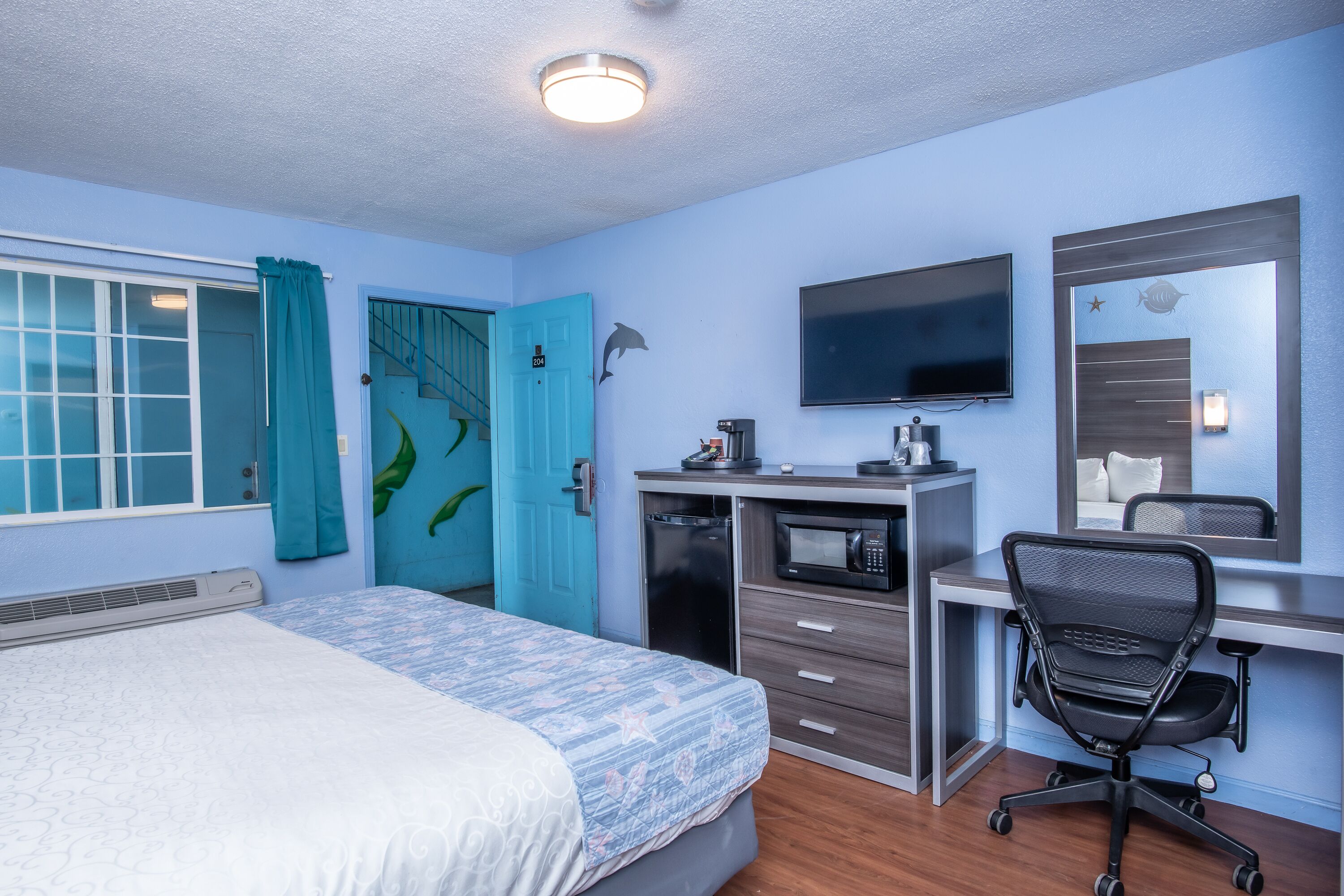 A hotel room with a bed, desk, chair, TV, and a microwave.