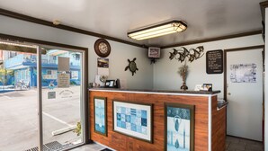 A reception area with a wooden counter, framed artwork, a clock, and a map on the wall. - Aqua Breeze Inn (Santa Cruz)