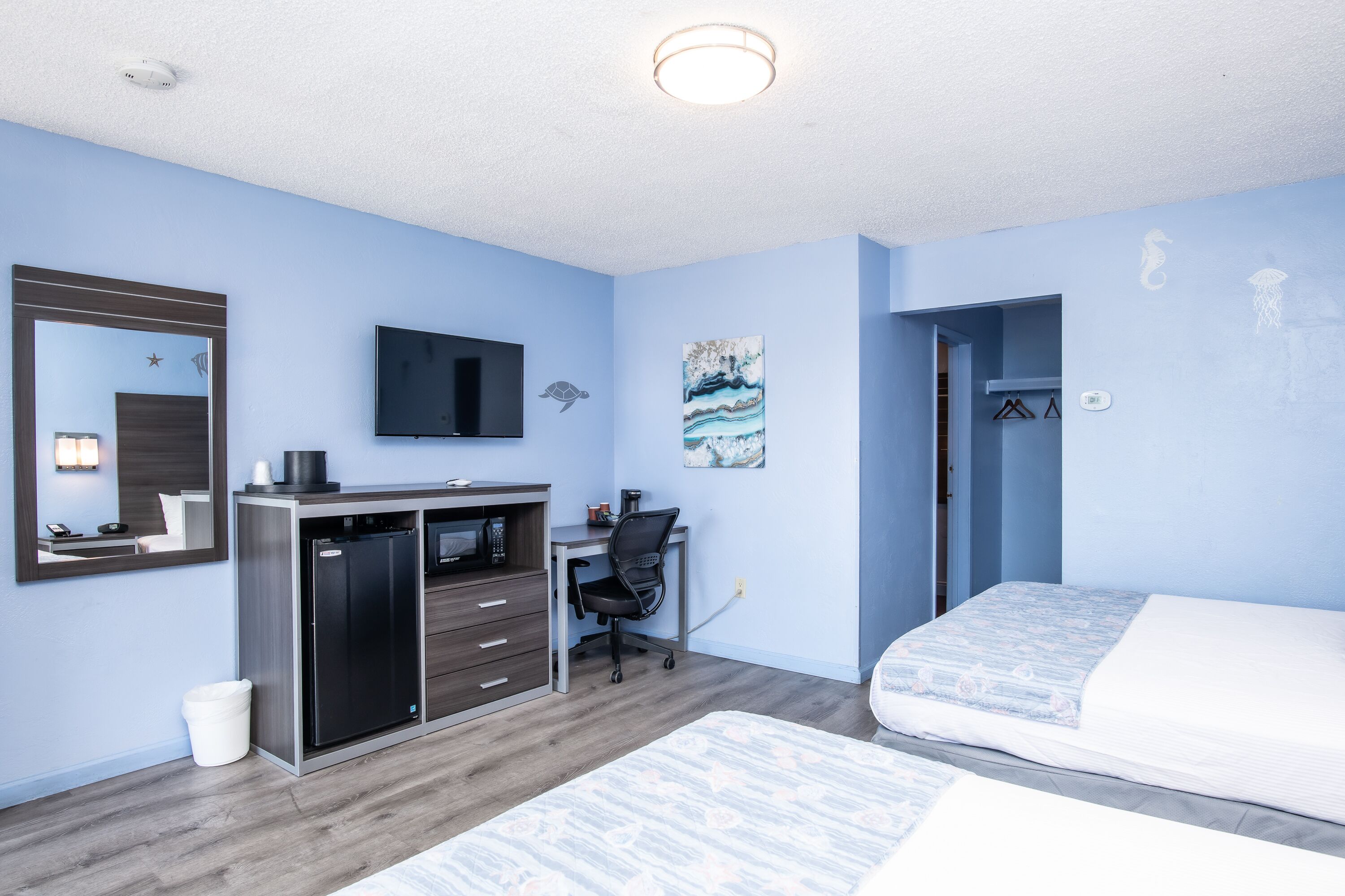 A modern hotel room with a bed, desk, and a small kitchenette.