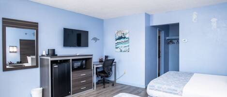 A modern hotel room with a bed, desk, and a small kitchenette.