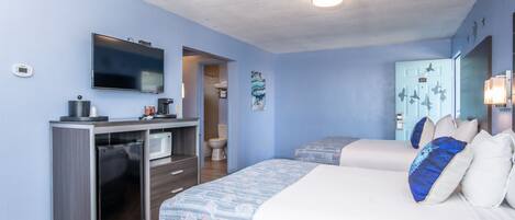 A hotel room with a bed, a desk with a refrigerator, a television, and a bathroom visible through an open door.