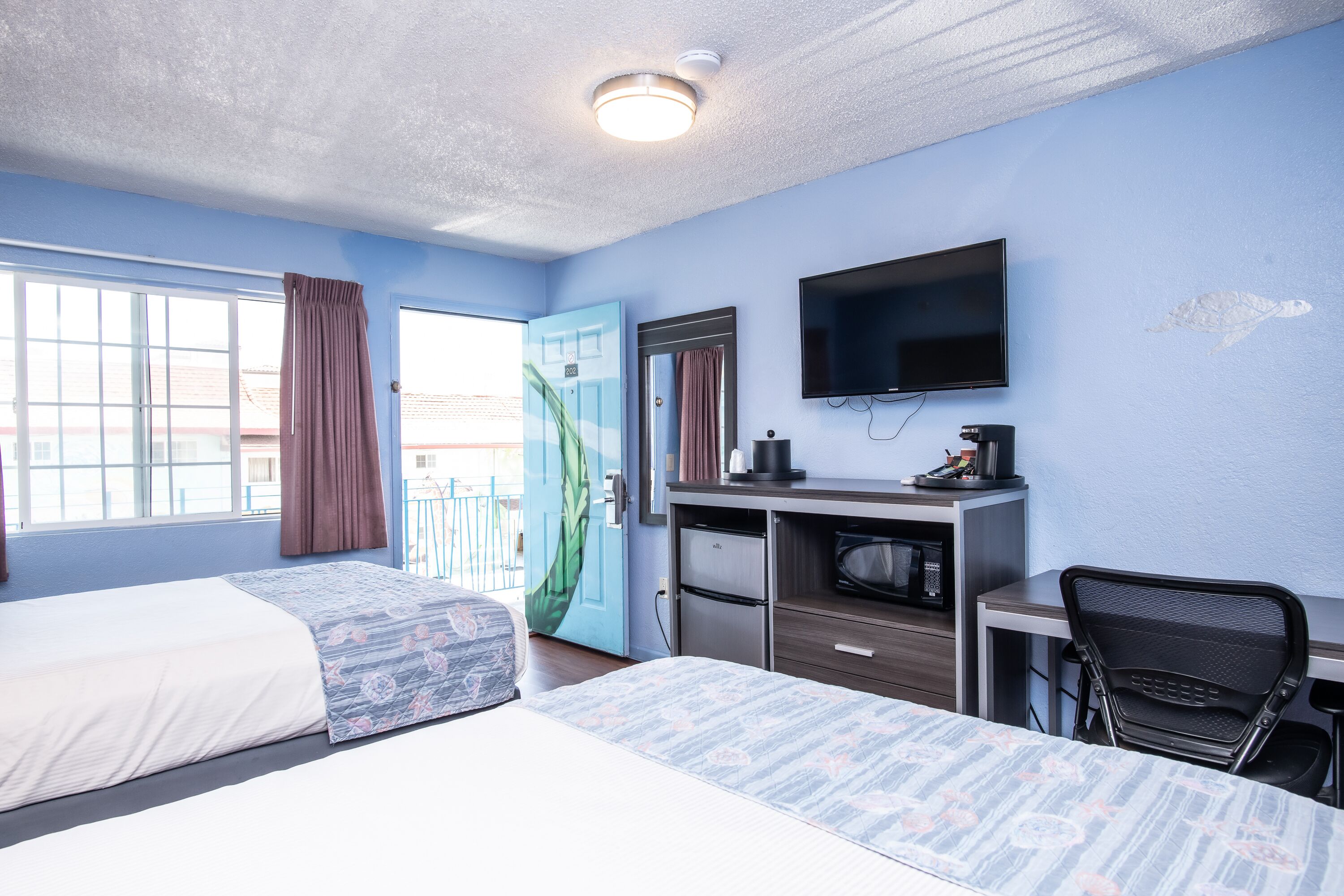 Une chambre d’hôtel avec deux lits, un bureau, une chaise, une télévision et une porte de salle de bain.