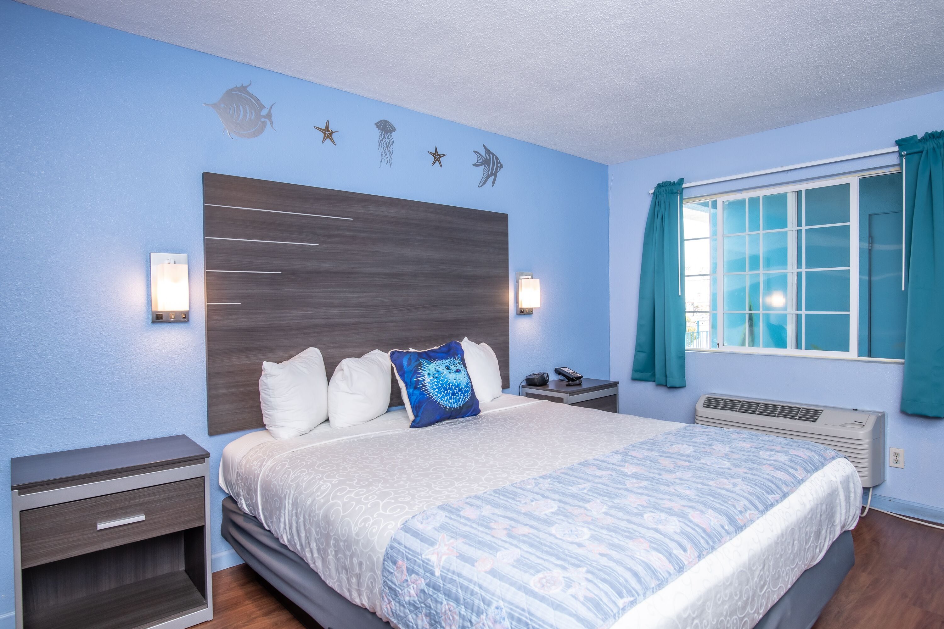 A bedroom with a large bed, a nightstand, a wall-mounted lamp, and a window with curtains.