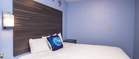 Une chambre à coucher avec un grand lit, une table de chevet, une lampe fixée au mur et des œuvres d’art décoratives accrochées au mur.