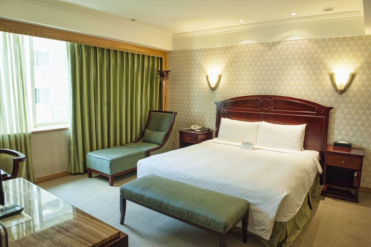 A hotel room with a large bed, a chair, a desk, and a nightstand.