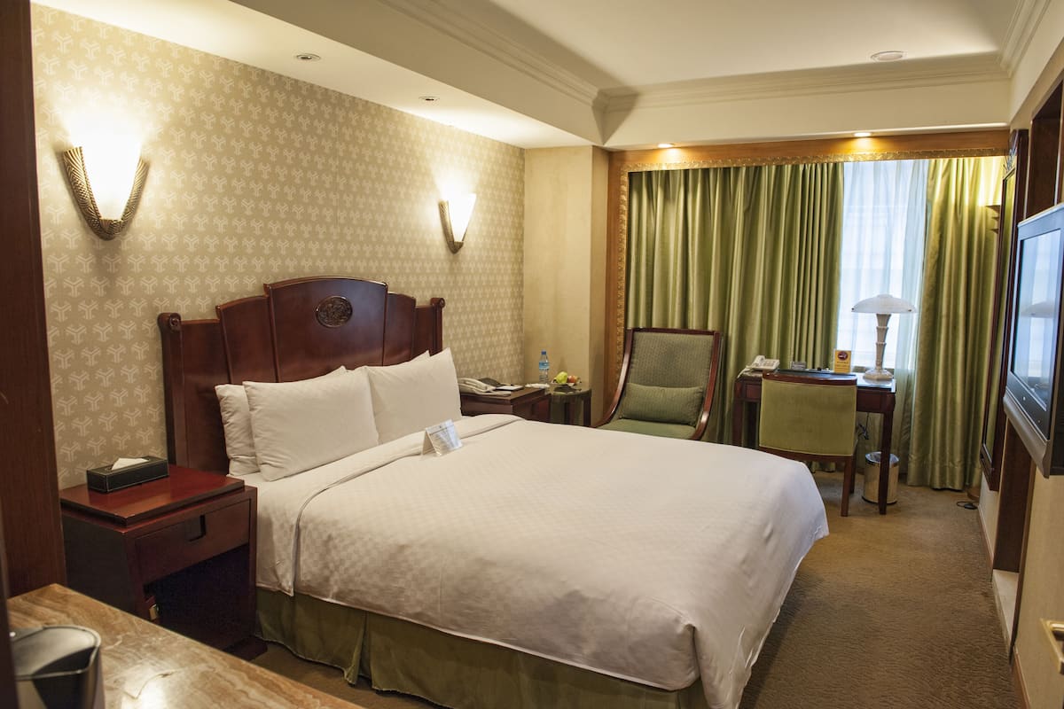 A hotel room with a large bed, a desk with a chair, a television, and a window with curtains.