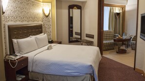A hotel room with a large bed, a bedside table with a phone, a mirror, a seating area with a table and chairs, and a TV on the wall. - Royal Palace Hotel (Taipei)