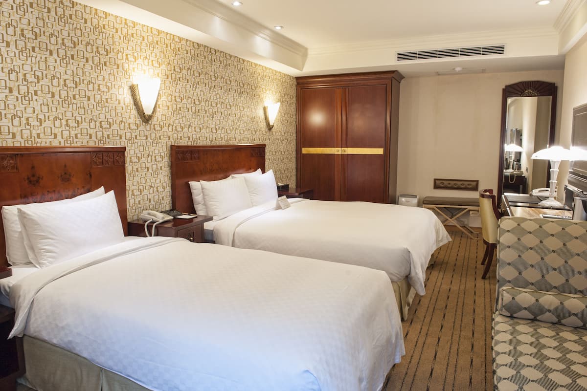 A hotel room with two beds, a desk, a chair, and a large mirror.