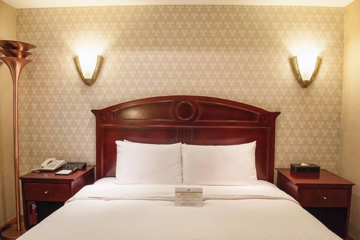 A hotel room with a large bed, two bedside tables, a telephone, and a lamp.