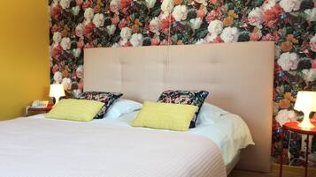 A hotel room with a floral wallpaper, a tufted headboard, and a bed with two pillows.