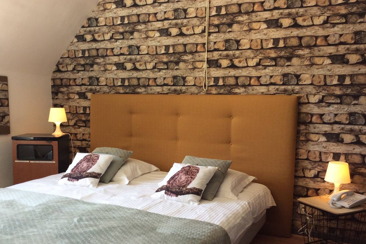A bedroom with a stone wall, a tufted headboard, and a bedside table with a lamp.