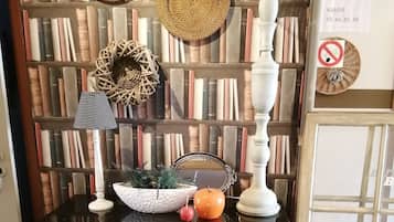 A room with a grey cabinet, a mirror, a white lamp, and a bookshelf filled with books.