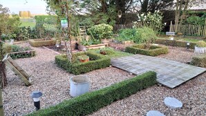 A well-maintained garden with a wooden deck, various plants, and a rustic bench. - Hotel Butler (Zuienkerke)