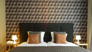 A hotel room with a tufted headboard, two bedside tables with lamps, and a large bed with a patterned bedspread. - Hotel Butler (Zuienkerke)