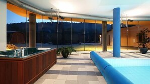 A modern indoor pool area with a hot tub, large windows, and a view of the surrounding landscape. - Hotel Ostrov (Tisa)