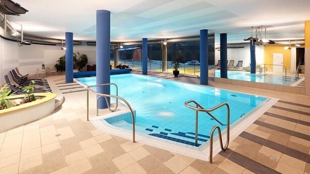 An indoor swimming pool with clear blue water, surrounded by blue pillars, and a tiled floor. - Hotel Ostrov (Tisa)