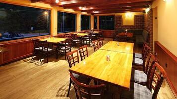A restaurant with wooden tables and chairs, large windows, and brick walls.